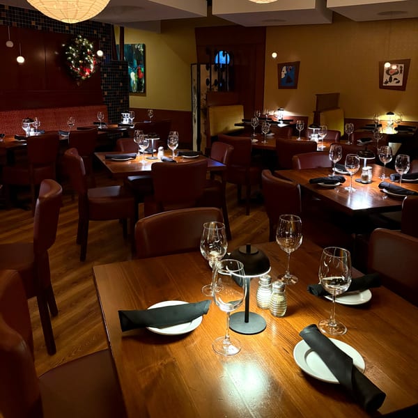 The dimly lit dining room of J Liu of Dublin, featuring set tables with wine glasses and brown leather chairs.