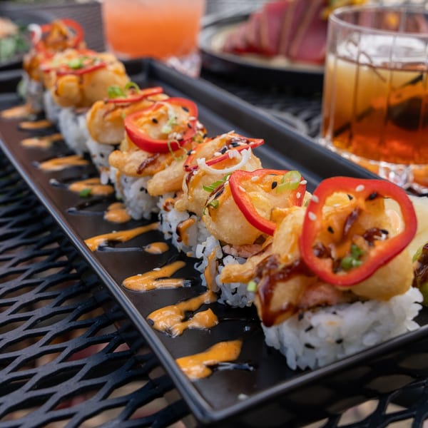 J Liu of Dublin's sushi roll with tempura, red peppers, and sauces on a black plate.