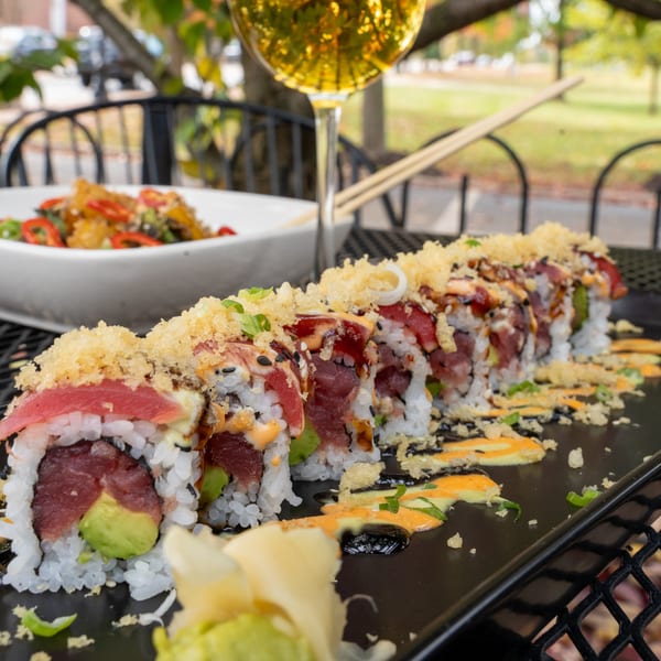J Liu of Dublin's tuna sushi roll with avocado, topped with crispy tempura flakes and sauces, on an outdoor table.