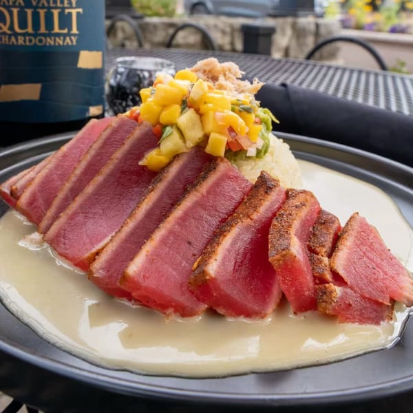 Seared tuna slices with mango salsa, crab, and a creamy sauce on a dark plate.