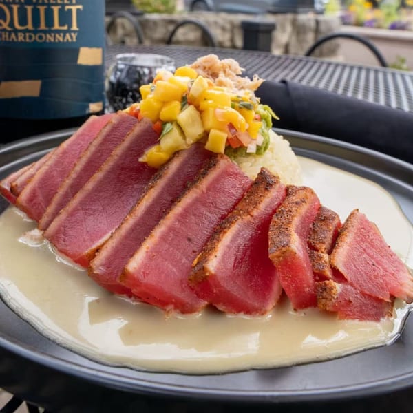 Seared tuna slices with mango salsa, rice, and a creamy sauce on a dark plate.