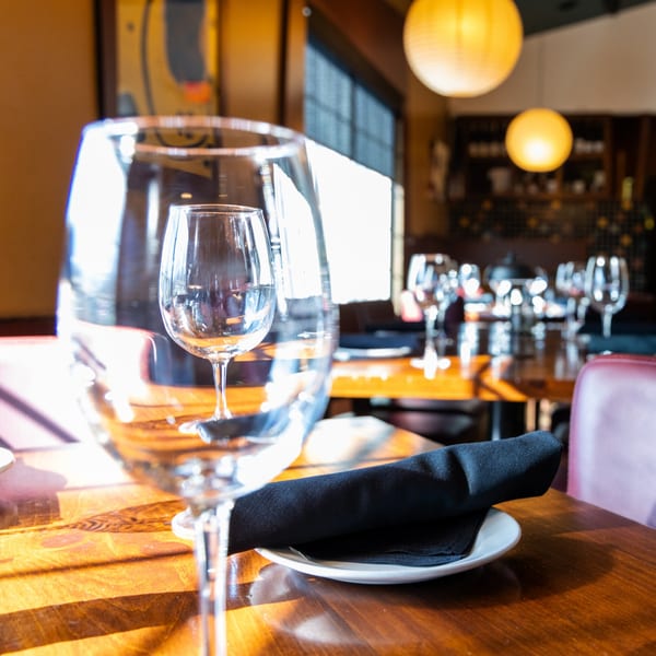 A J Liu of Dublin dining table set with wine glasses and a black napkin, bathed in sunlight.