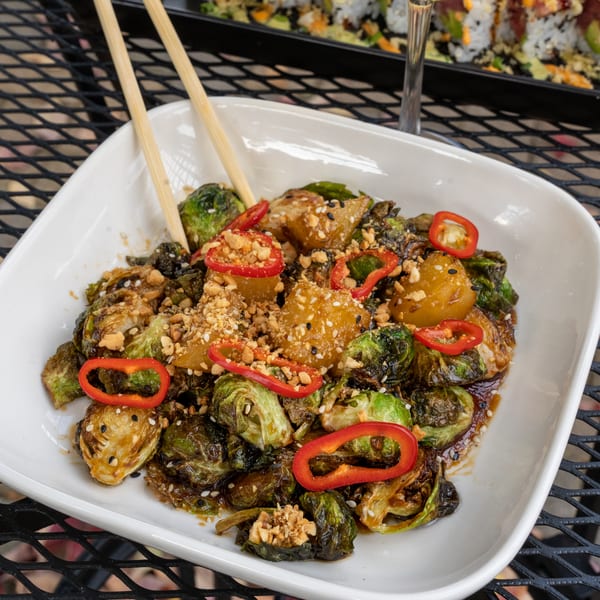 A white rectangular dish of J Liu's roasted Brussels sprouts with red peppers, peanuts, and sesame seeds.